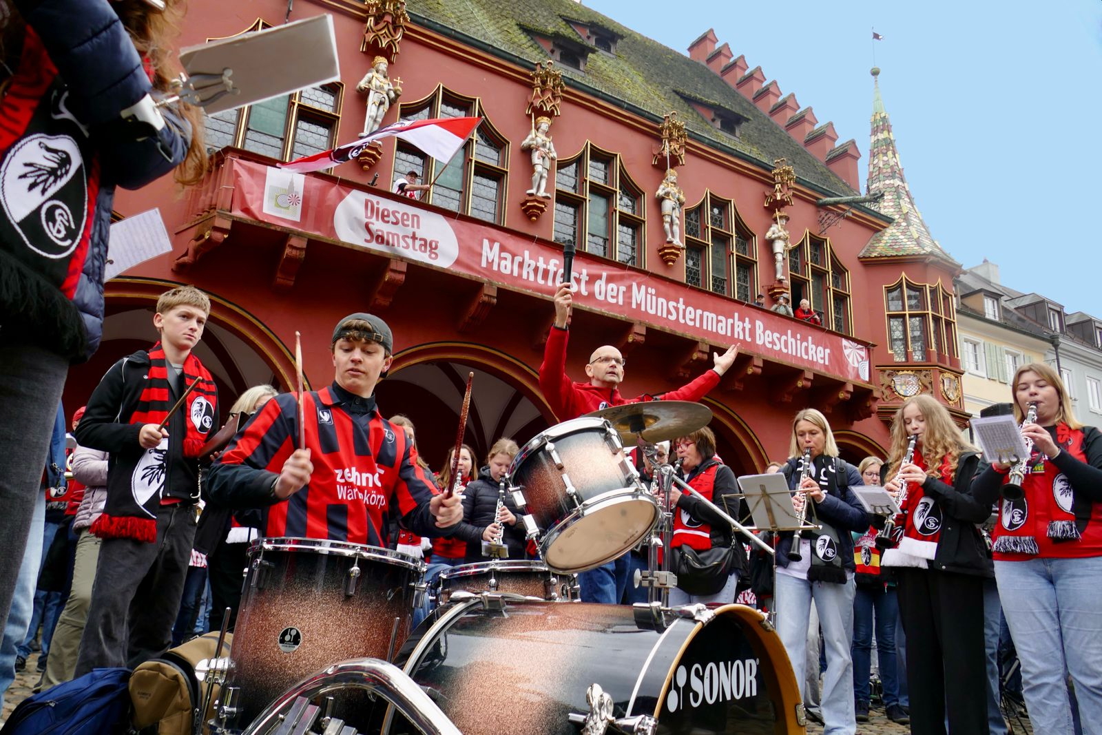 Musiker mit SC-Freiburg-Schals am Schlagzeug vor dem Historischen Kaufhaus am Münstermarkt – Blasmusik-Flashmob 2026
